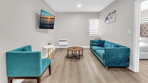 A modern living room with teal sofas, a round coffee table, and a large painting of a sunset. - Boutique 2BR in Bay Harbor Islands close to beach, shops, and dining (Bay Harbor Islands)