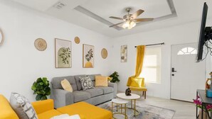 Un salon avec un canapé gris, un fauteuil jaune et un ventilateur de plafond.