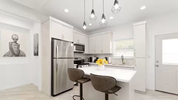 Une cuisine moderne avec des meubles blancs, des appareils en acier inoxydable et des luminaires suspendus.