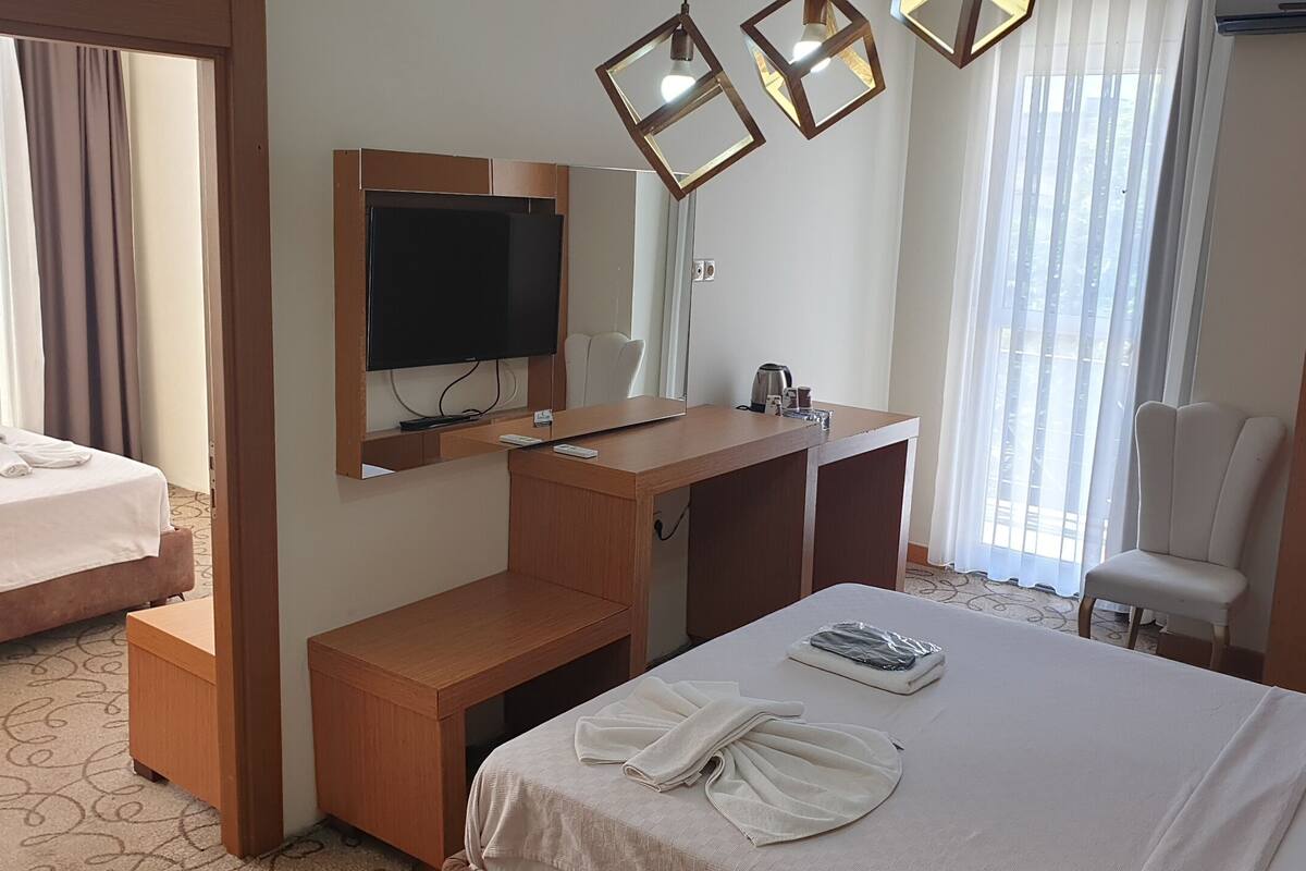 Ett hotellrum med en säng, ett skrivbord med en platt-TV, en stol och ett fönster med gardiner.