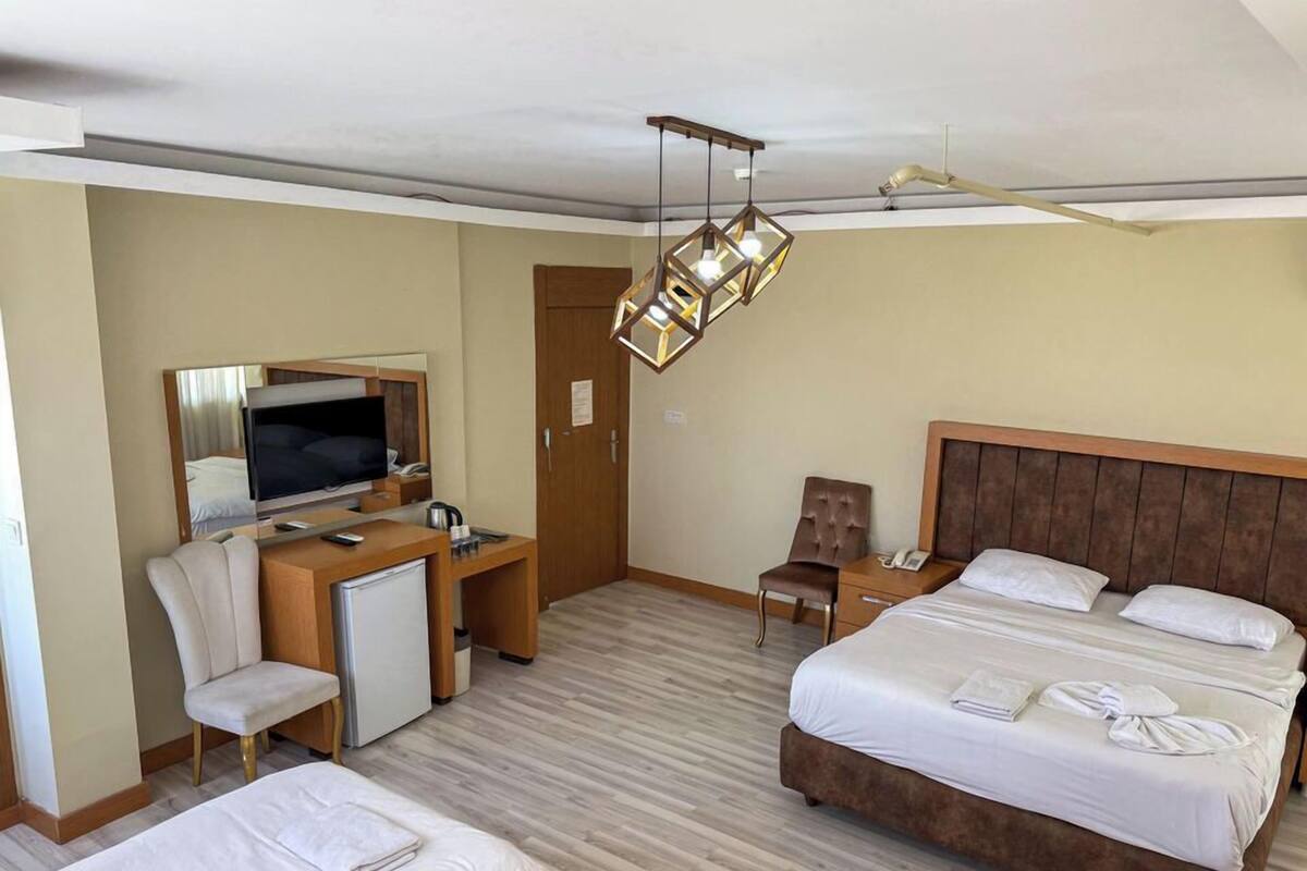 Ett hotellrum med en säng, ett skrivbord med en dator, en stol, ett litet kylskåp och en tv.