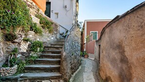 Un escalier étroit en pierre mène à un bâtiment à la façade rustique, entouré de verdure et de plantes en pot.