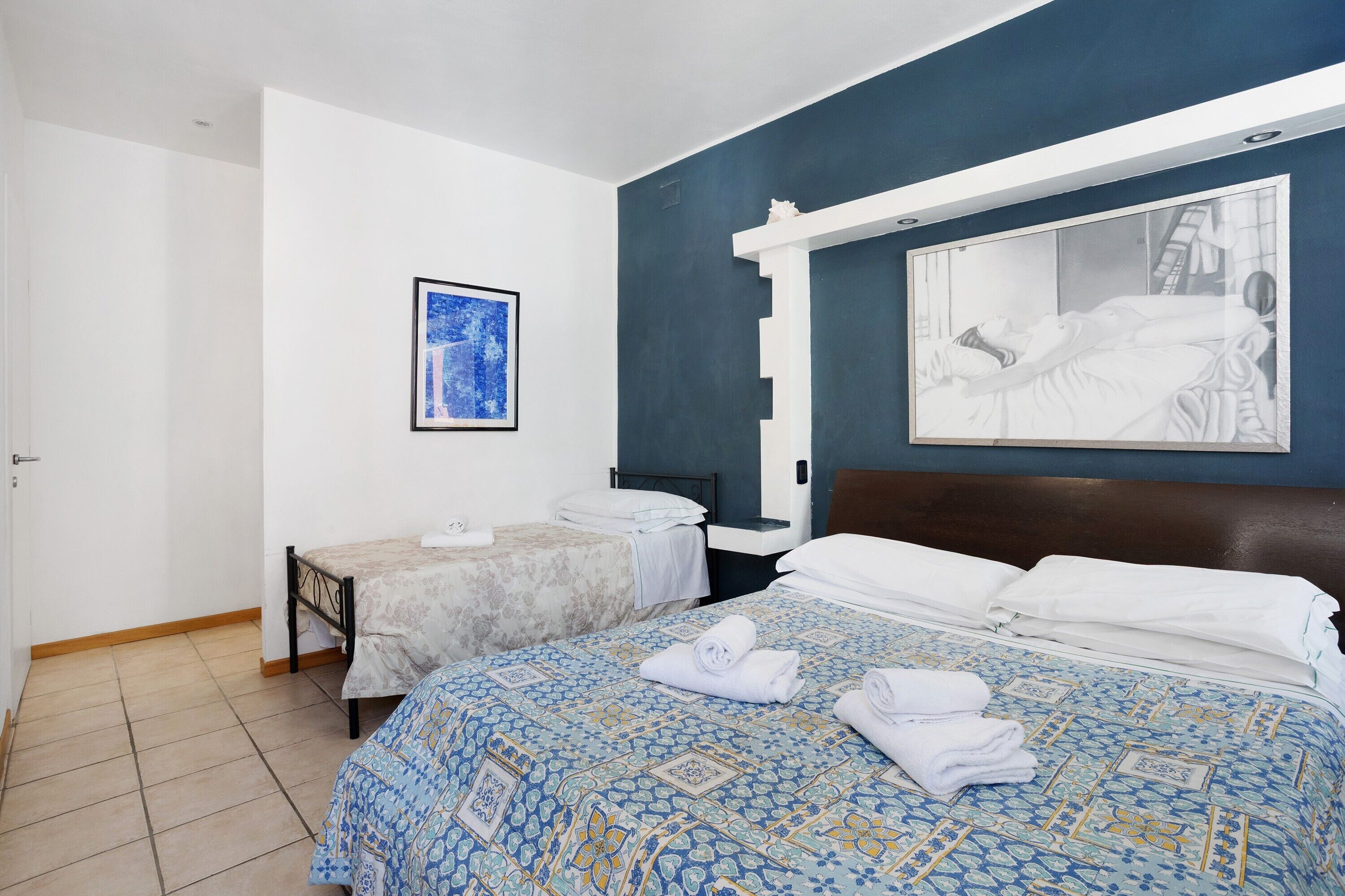 Een hotelkamer met twee bedden, een groot schilderij aan de muur en een ingelijst plaatje boven de bedden.