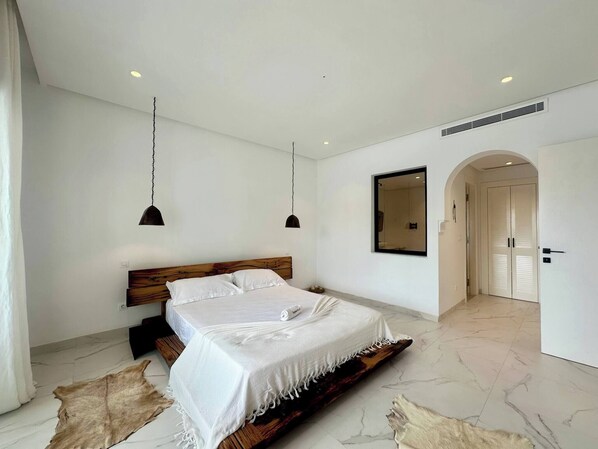 A bedroom with a bed, two pendant lights, a mirror, and a door. - Appartement Serena Beachfront Hammamet (Hammamet)