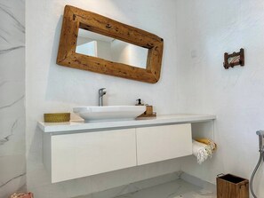 A bathroom with a white vanity, a wooden-framed mirror, a white sink, and a shower area. - Appartement Serena Beachfront Hammamet (Hammamet)