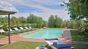 Zona de piscina amb gandules, taula amb un vas i un got, i zona d'estar coberta.