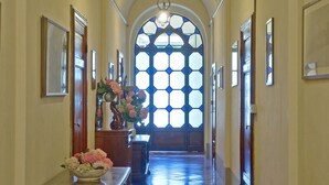 Un passadís amb una banca de fusta, un ram de flors i un gran finestral apuntat amb disseny de vitrall.