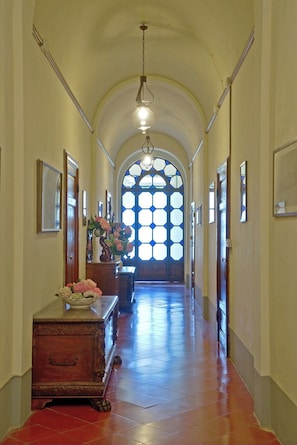 Un pasillo con un banco de madera, un jarrón de flores y un amplio ventanal de arco con motivos de vitral.