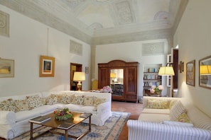 Un salón espacioso con un sofá blanco, un sillón a rayas, un aparador de madera y una estantería.