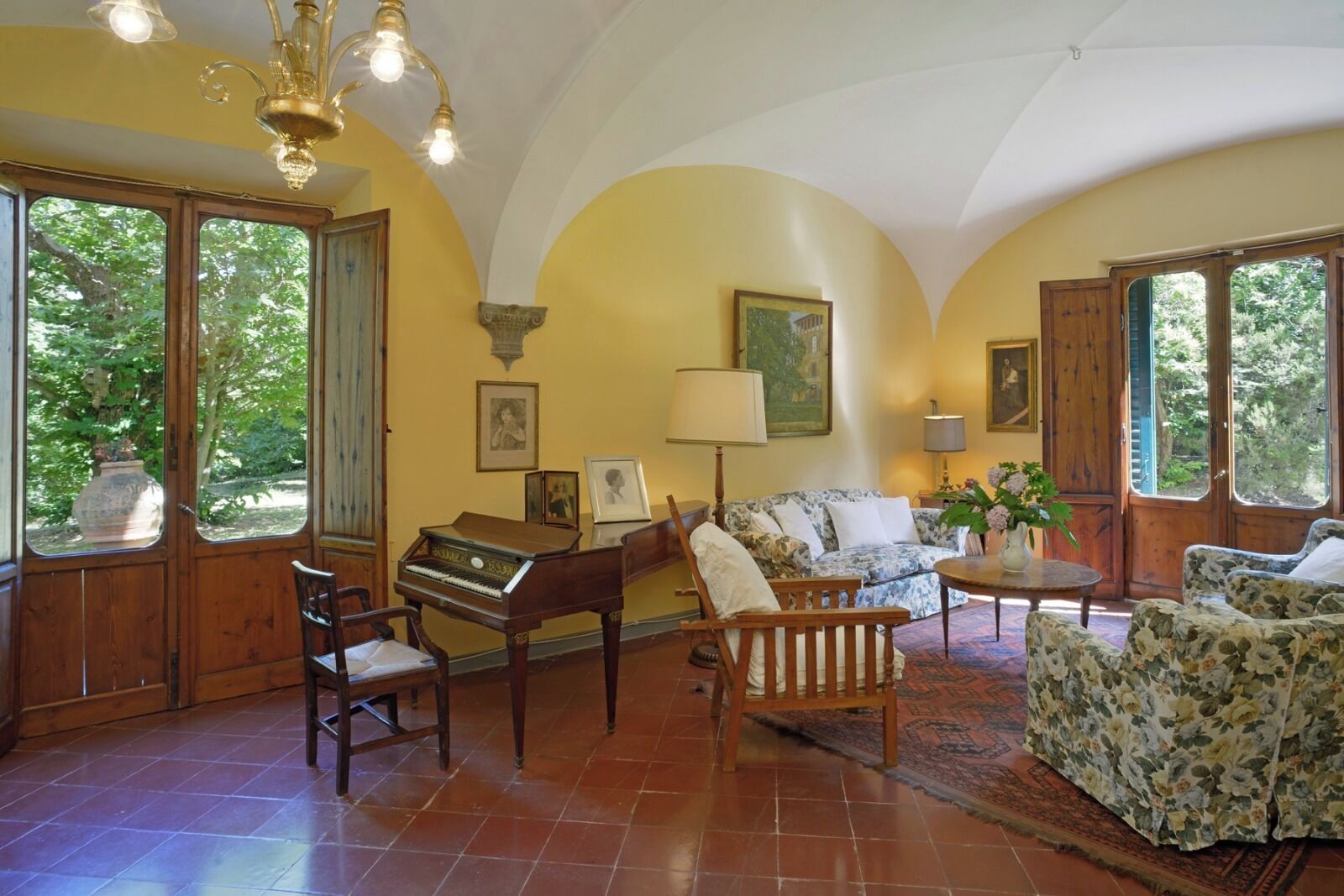 Una habitación con un piano, un sofá, una silla, una lámpara y un jarrón con flores.