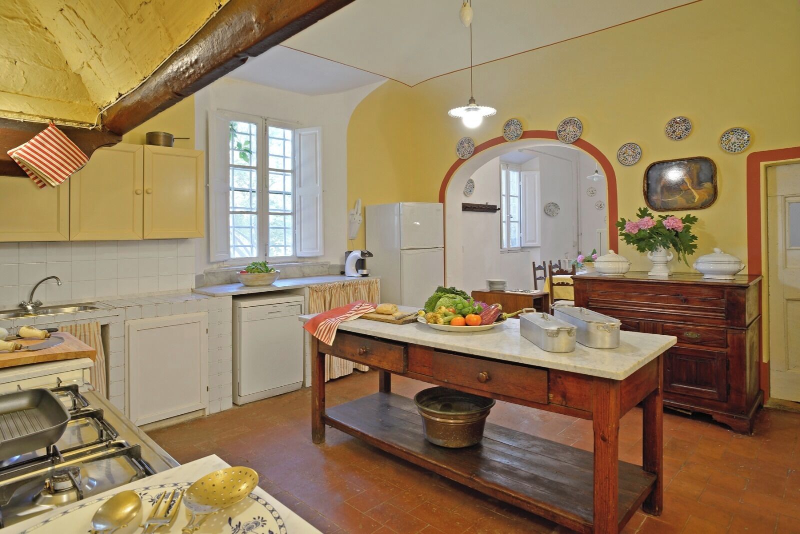 Una cocina con armarios de madera, una mesa de comedor con mantel rojo, un fregadero y una estufa.