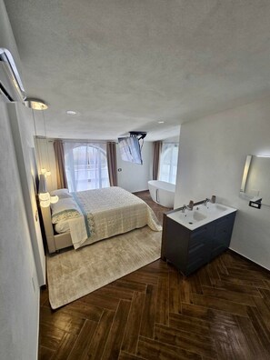 Quarto de hotel moderno com cama, banheiro com banheira e um espelho grande.