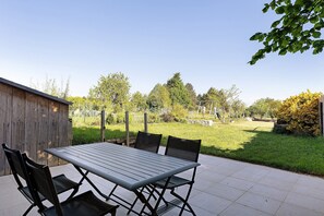 Une terrasse extérieure avec une table et des chaises, une clôture en bois et une cour verdoyante avec des arbres.