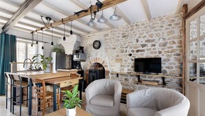 Un intérieur rustique avec des poutres apparentes, des murs en pierre, une cheminée, un téléviseur et des sièges.