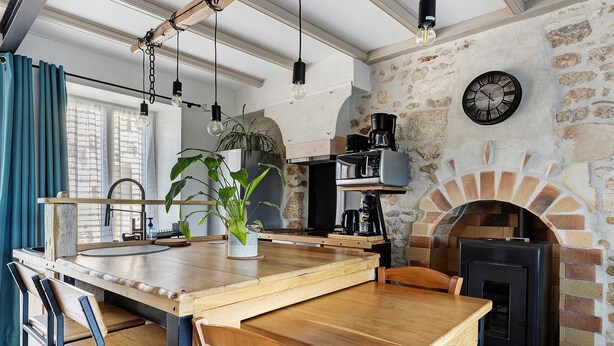 Une cuisine rustique avec une table en bois, des chaises, une machine à café et une cheminée en briques.