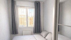 A bedroom with a bed, a window with curtains, a radiator, and a ceiling light fixture. - Haven of peace (Montpellier)