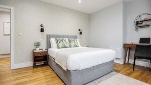 Un dormitorio moderno con cama gris, mesitas de noche de madera, un escritorio y una silla.