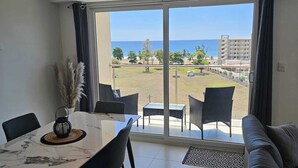Ein modernes Wohnzimmer mit Essbereich, große Schiebeglastüren, die auf einen Balkon mit Blick auf das Meer und den Strand führen.