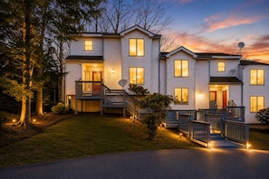 A two-story residential building with a front porch, satellite dish, and a well-lit driveway. - Mystic Duo | 2 Homes Side-by-Side | Sleeps 14 (Lake Harmony)