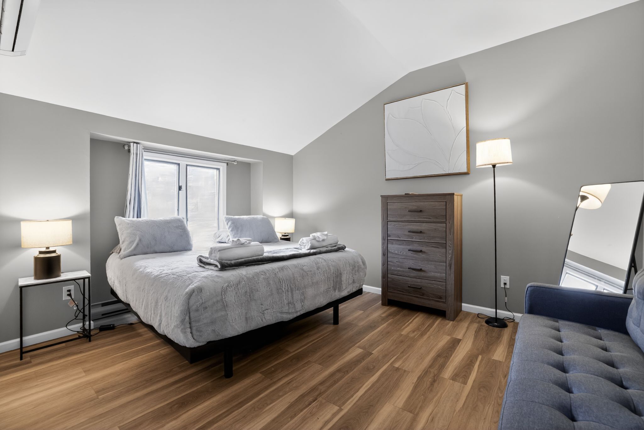 Een slaapkamer met een bed, nachtkastjes, een kaptafel, een vloerlamp en een schilderij aan de muur.