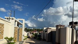A residential street with houses, a dirt road, and a clear sky. - Tranquil 3-bedroom apartment with AC in Dar es Salaam (Dar es Salaam)