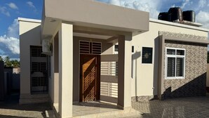 A modern building with a covered entrance, a visible door, and a paved driveway. - Tranquil 3-bedroom apartment with AC in Dar es Salaam (Dar es Salaam)