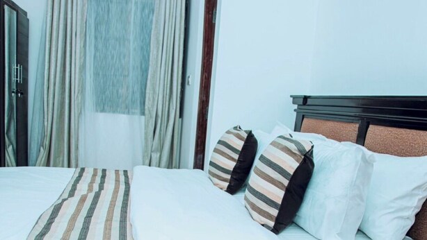 A neatly made bed with striped bedding, a headboard, and two pillows with striped patterns. - Tranquil 3-bedroom apartment with AC in Dar es Salaam (Dar es Salaam)