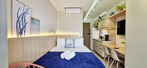 Ein Hotelzimmer mit Bett, Schreibtisch, Stuhl, Fernseher und einer Küchenzeile.