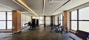 Ein Fitnessraum mit Trainingsgeräten, großen Fenstern und gefliestem Boden.