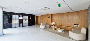 Eine moderne Lobby mit einem Marmor-Empfangstresen, einer Sitzecke mit rundem Couchtisch und einer Holzwand mit einem angebrachten Kunstwerk.
