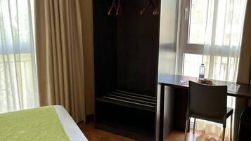 A hotel room with a bed, a desk, a chair, a wardrobe, and a window with curtains.