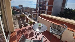 Un balcón con mesa y sillas, plantas en macetas y vistas de edificios circundantes.