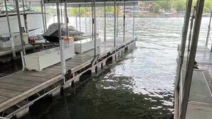 Een boot aangemeerd aan een steiger, met een overdekt dek, een barbecue en een klein wit gebouw.