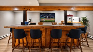 Eine Bar mit Holztresen, vier Barhocker, einem Fernseher, der ein Baseballspiel zeigt, und einem Kühlschrank.