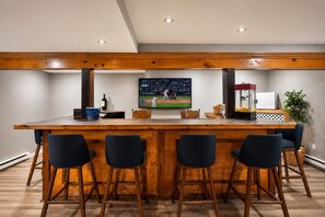 A bar area with a wooden bar counter, four bar stools, a television displaying a baseball game, and a refrigerator. - Mystic Escape + Pool Passes Near Big Boulder (Lake Harmony)