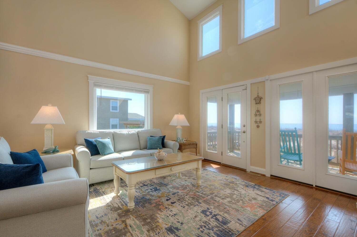A spacious living room with a large window, a white sofa, a coffee table, and a patterned rug.