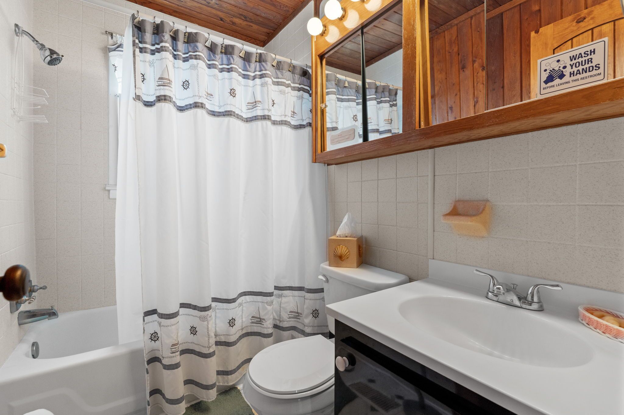 A bathroom with a bathtub, toilet, sink, and a mirror with a 'WASH YOUR HANDS' sign.