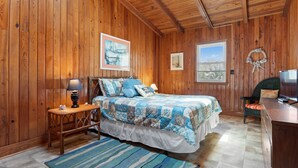 Ein Schlafzimmer mit Holzwandverkleidung, einem Bett, einem Nachttisch, einer Lampe und Blick ins Freie.
