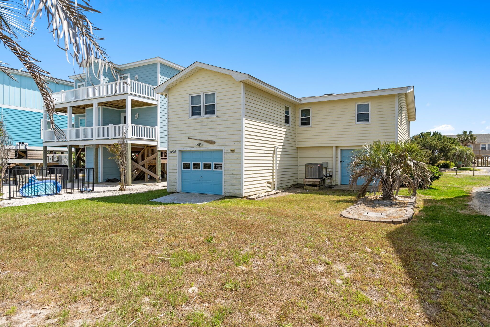 A two-story house with a blue garage door, a balcony, and a small garden area.