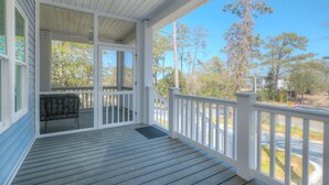 Eine überdachte Veranda mit einer Bank, weißen Geländern und Blick auf Bäume und eine Straße.