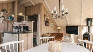 A cozy cabin interior with a dining table, chairs, a kitchen area, a fireplace, and a television. - 5 Person Holiday Home in Nakskov (Nakskov)