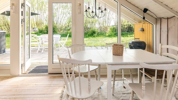A dining area with a white table and chairs, a chandelier, and a view of the outdoors. - 5 Person Holiday Home in Nakskov (Nakskov)