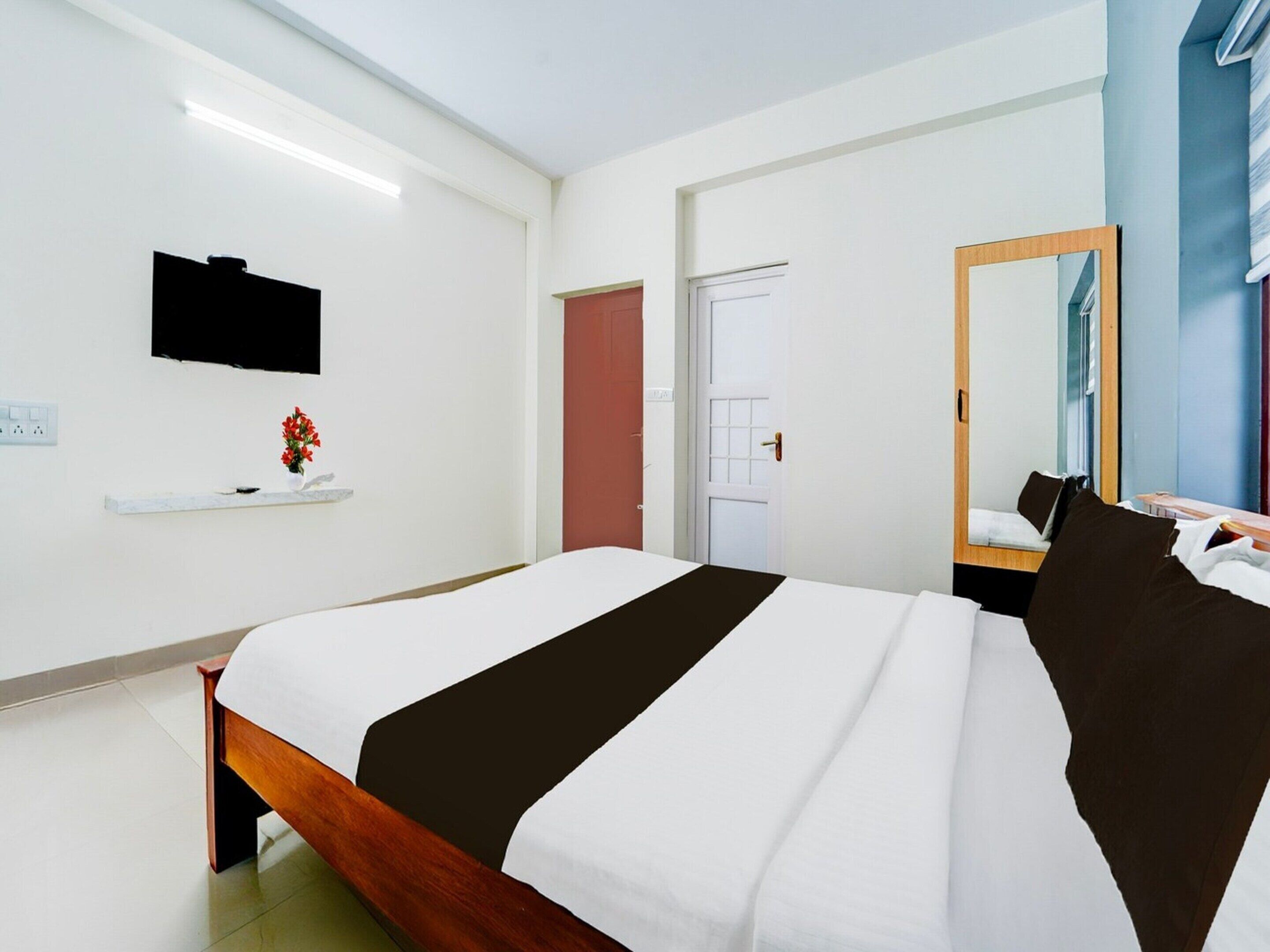 A hotel room with a bed, a TV mounted on the wall, a door, and a mirror.