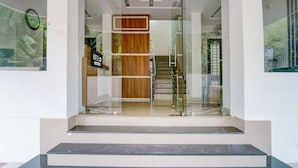 A hotel entrance with a glass door, a wooden panel, and a staircase leading inside.