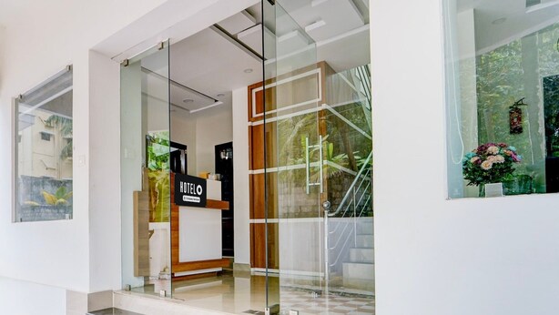 A hotel entrance with a reception desk, glass doors, and a view of greenery outside.