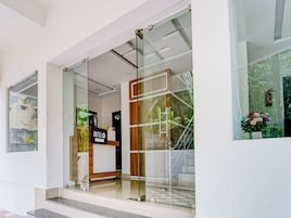 Entrada de un hotel con mostrador de recepción, puertas de vidrio y vistas al exterior con vegetación.