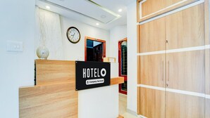 A hotel reception desk with a clock, a sign indicating it's company-serviced, and a wooden wardrobe.