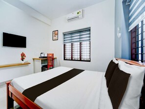 Habitación de hotel con cama, escritorio, silla, televisor, aire acondicionado y ventana con persianas.