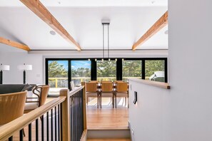 Ein modernes Interieur mit Holzbalken, einer Treppe und einem Essbereich mit Stühlen und Tischen.