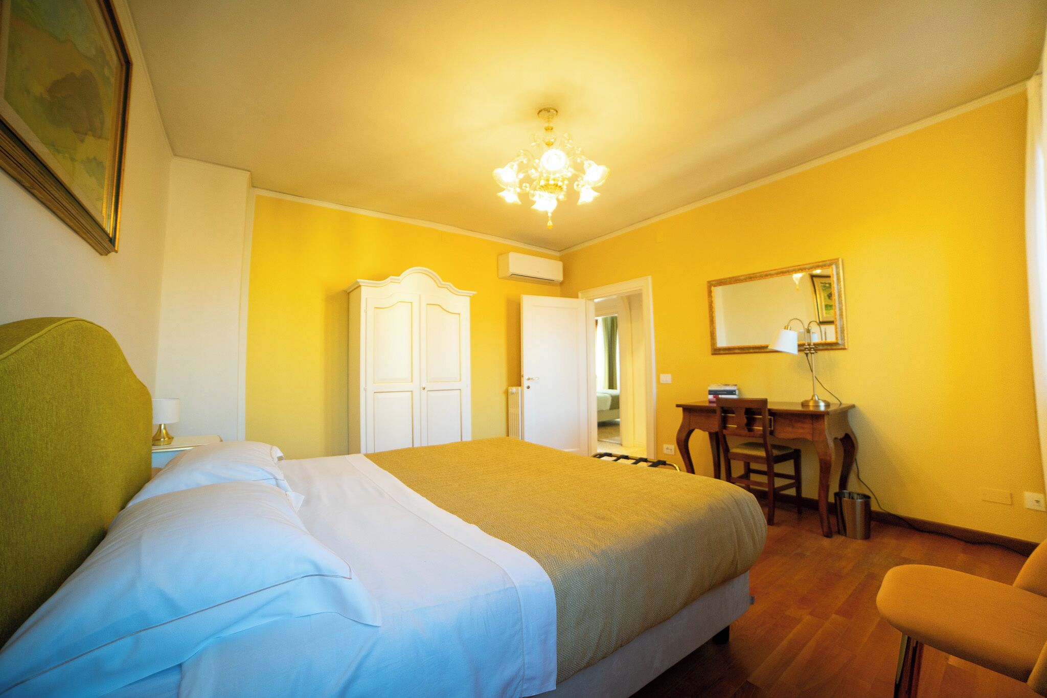 A hotel room with a bed, a desk, a chair, a wardrobe, and a chandelier.